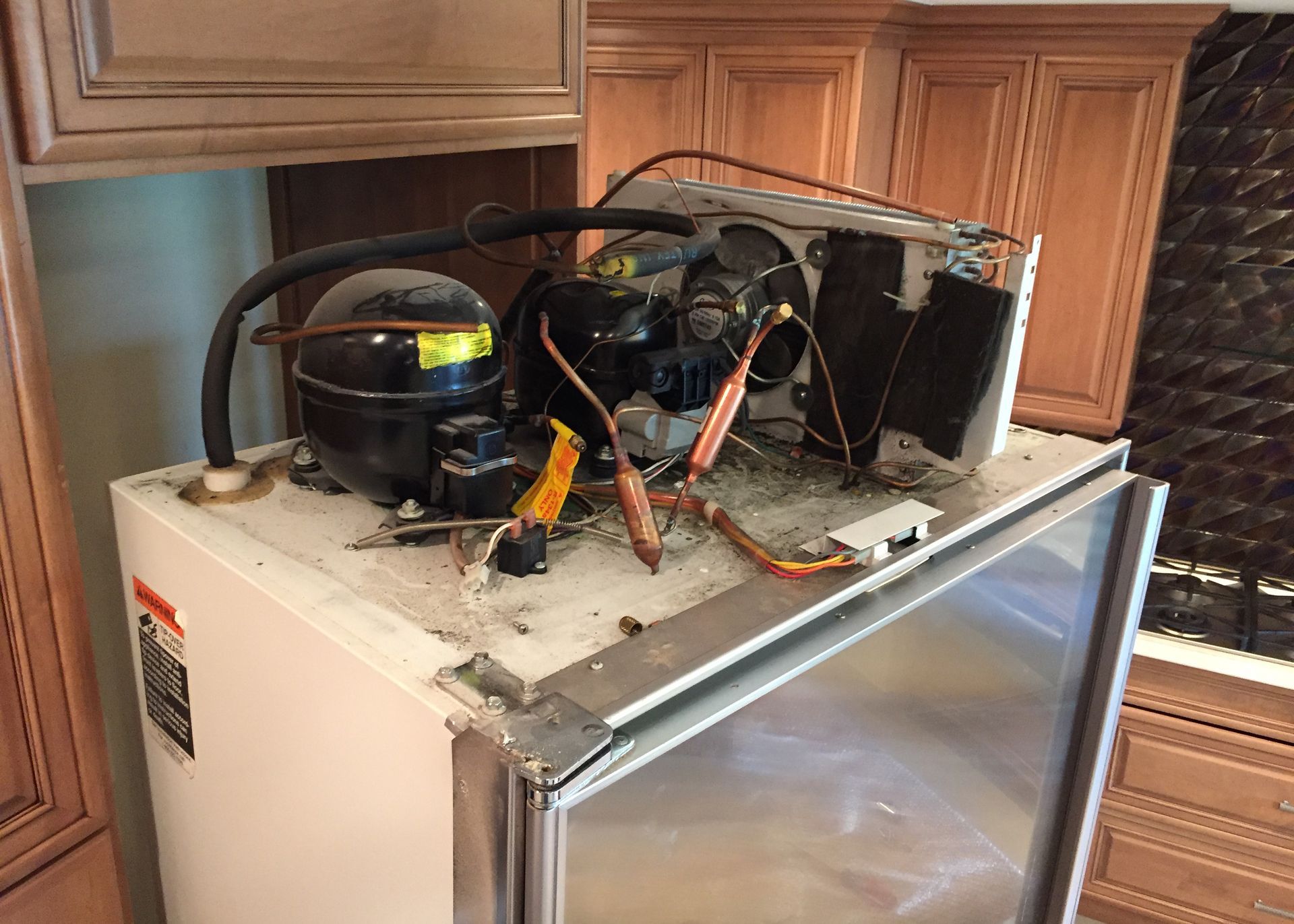 The inside of a refrigerator is being repaired in a kitchen.