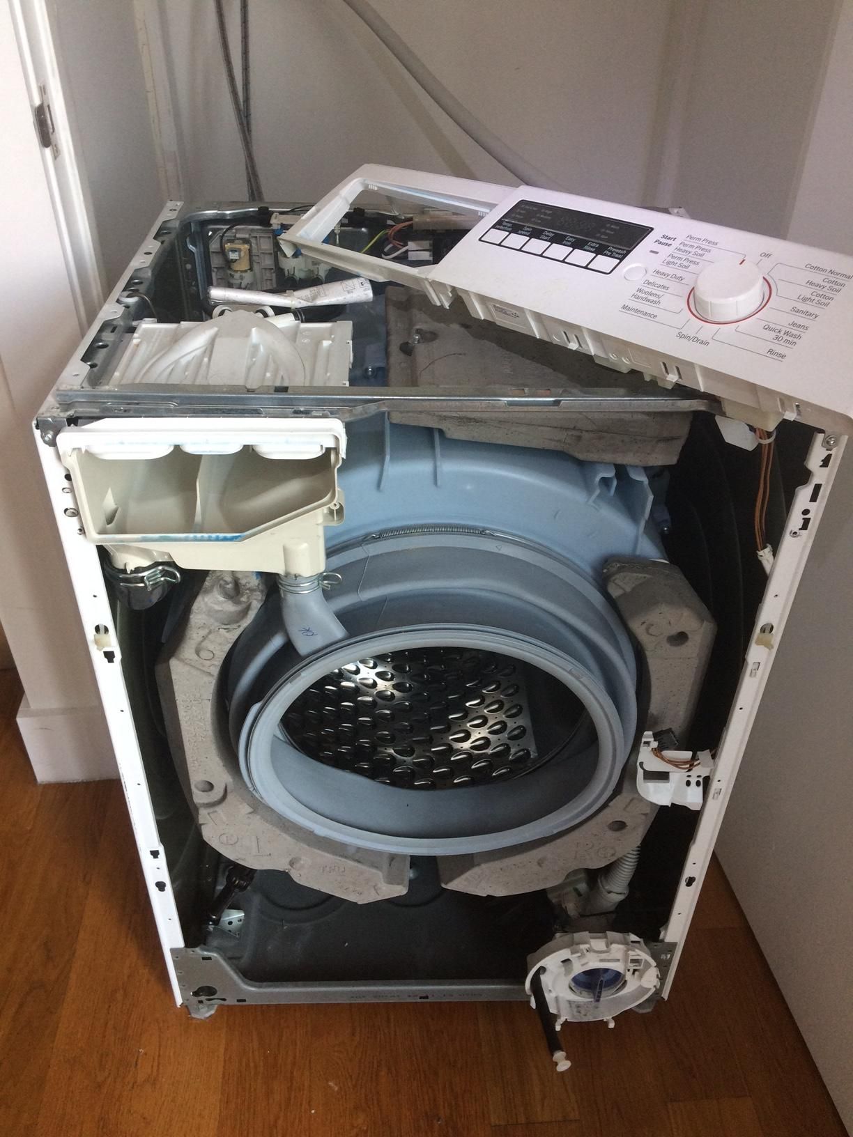A broken washing machine is sitting on a wooden floor in a room.