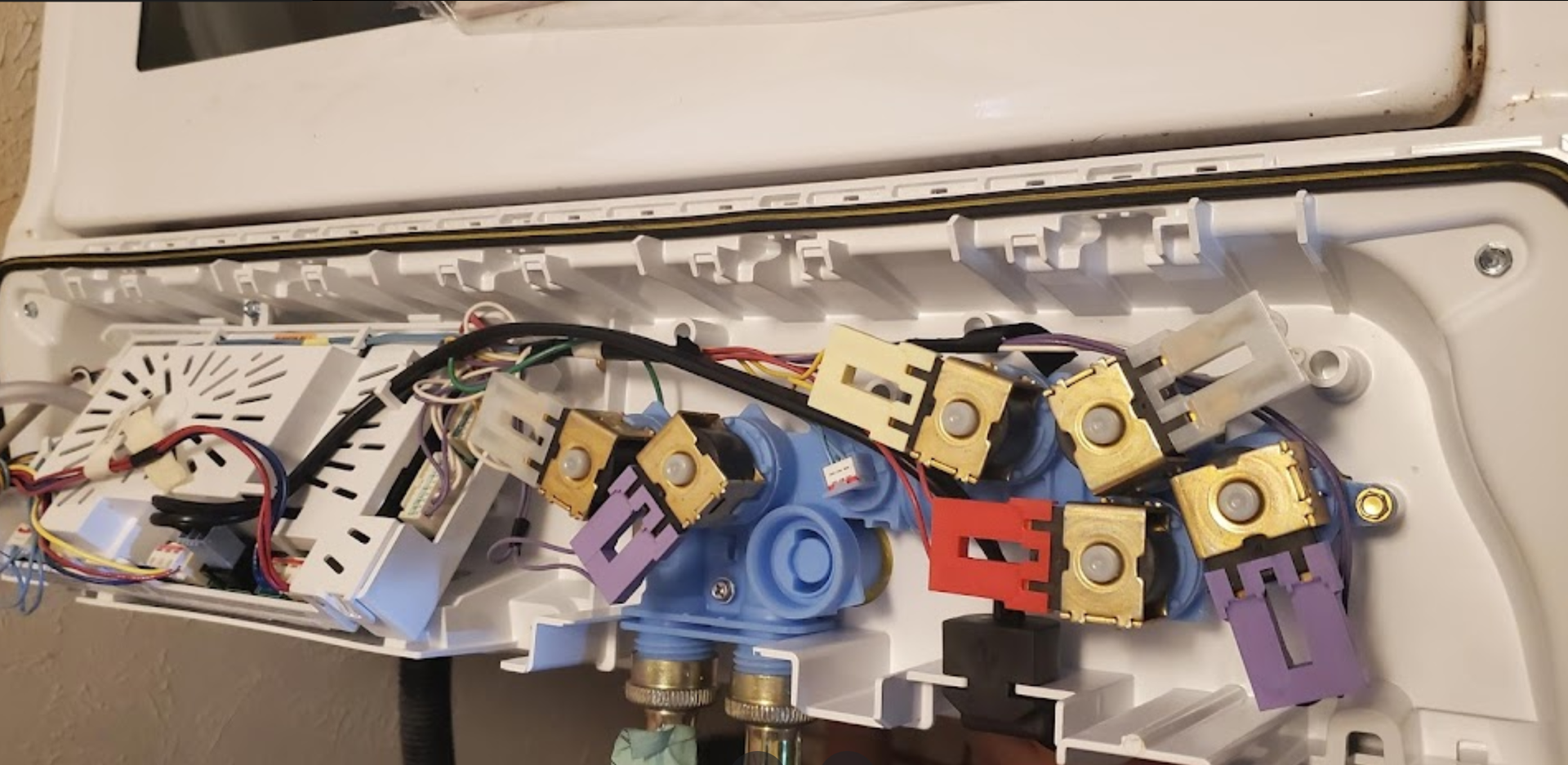 The inside of a washing machine with a lot of wires and valves.
