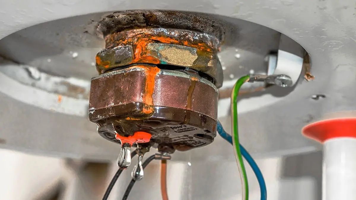 A close up of a rusty water heater with wires coming out of it.