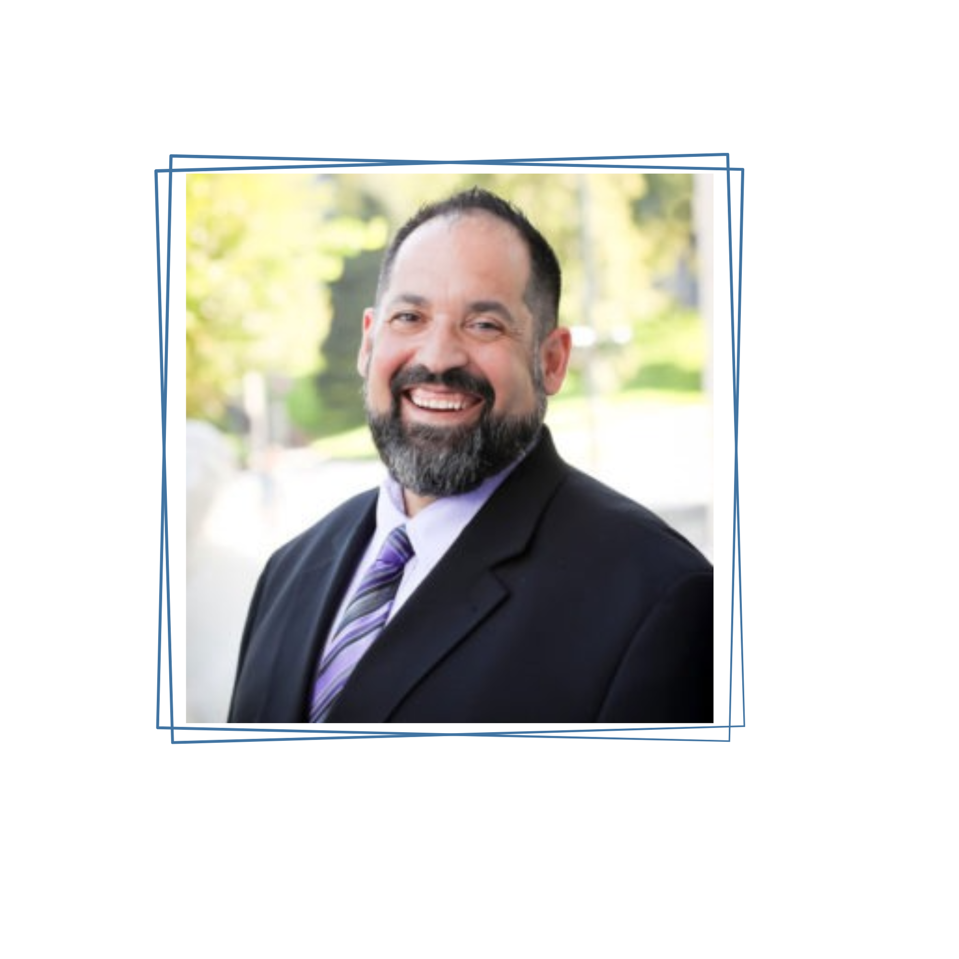 A person with a beard, wearing a suit and purple-striped tie, smiling outdoors in a headshot portrait.