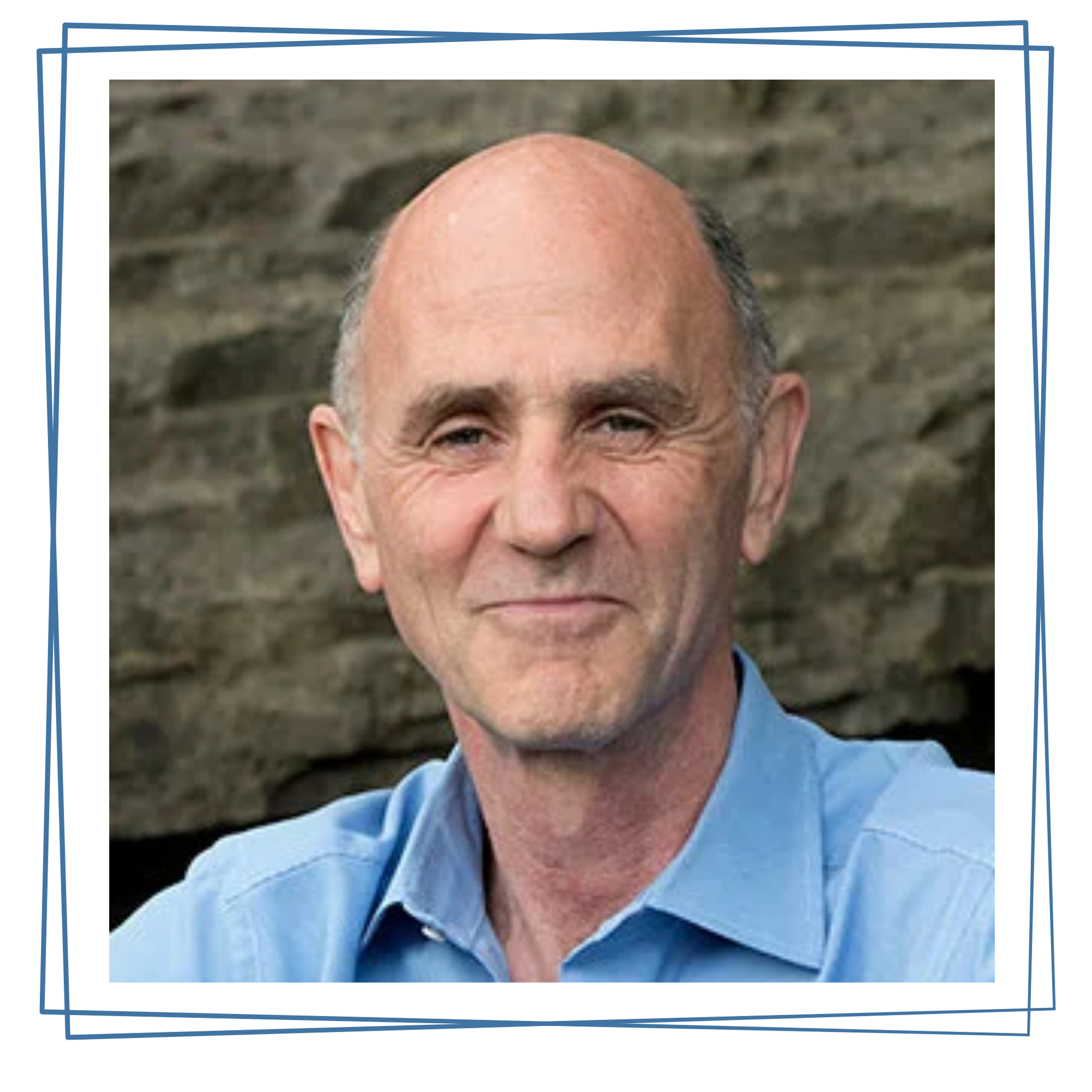 Smiling man in a light blue shirt against a stone wall backdrop