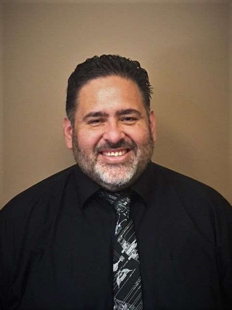 Man in black shirt and tie, smiling, indoors.