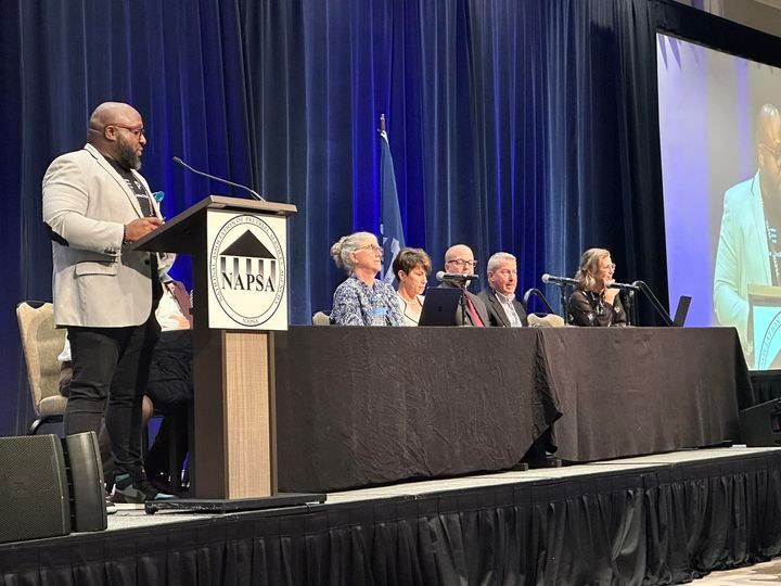 Blue and white trade show booth with cylindrical display and small table.