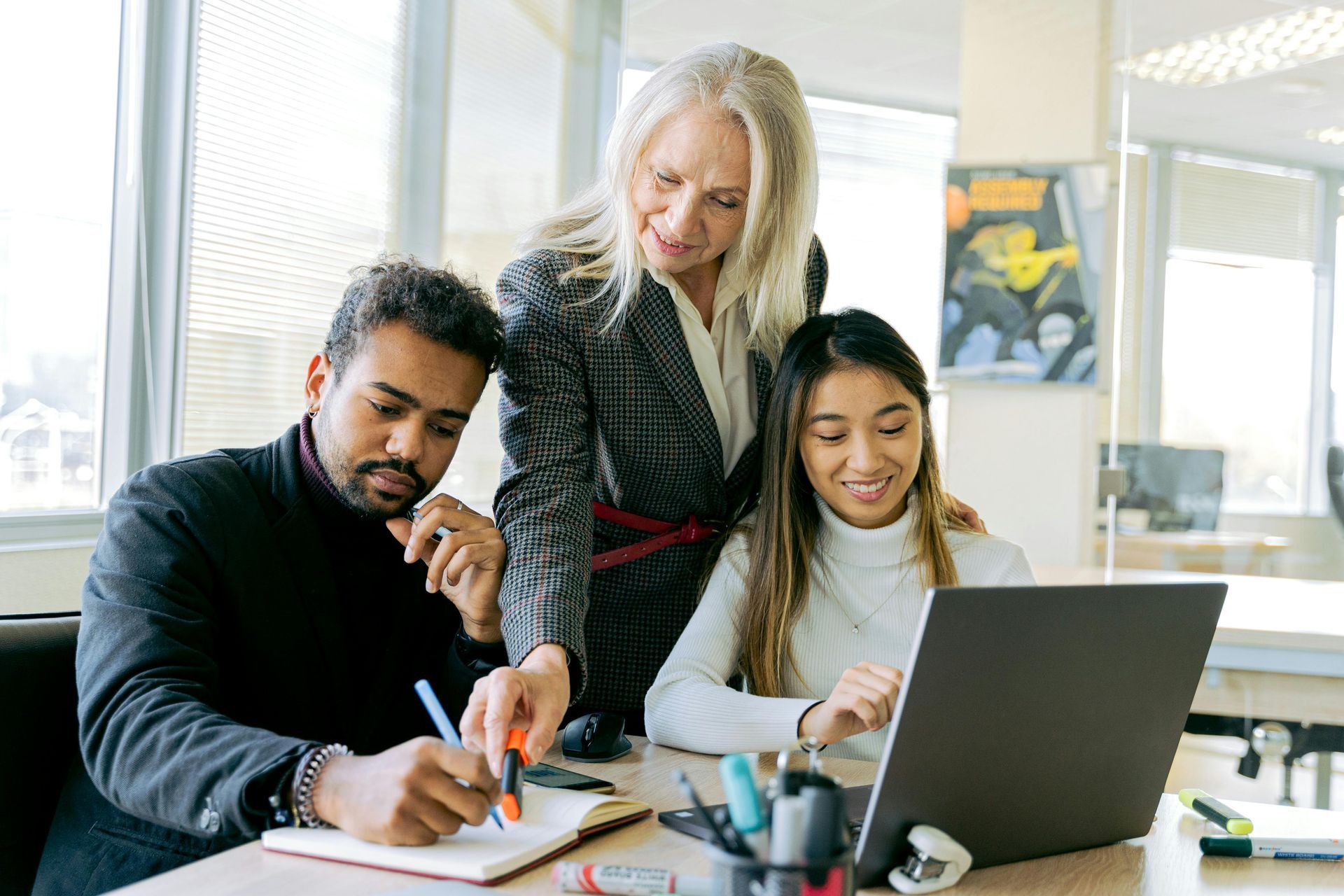 Three people collaborating at a table with a laptop and notebook in an office.