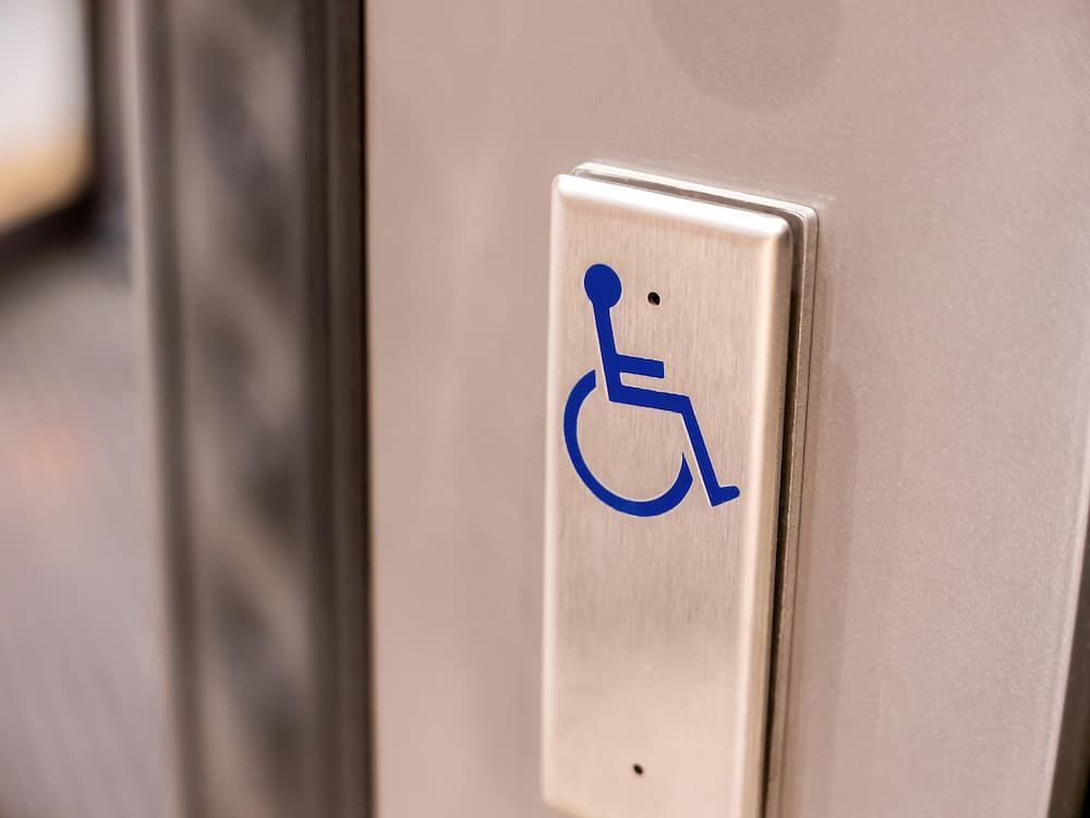 Stainless steel ADA automatic door opener push plate with blue handicap accessibility symbol.