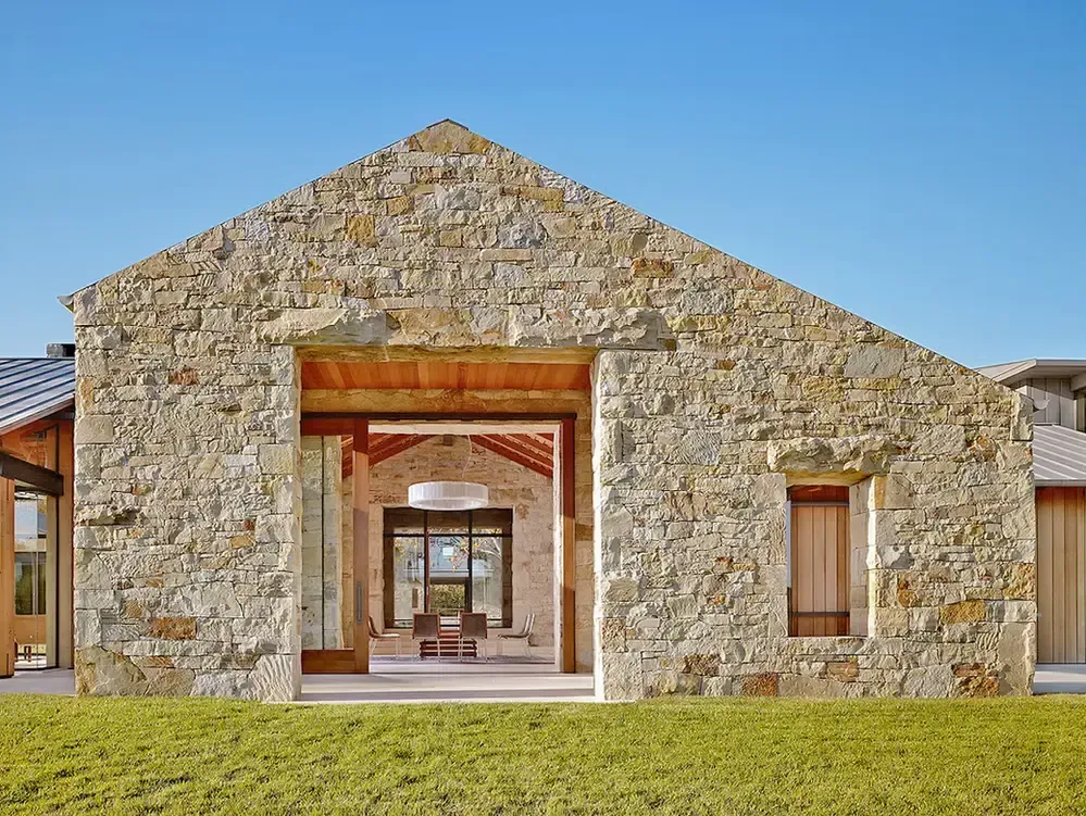 A stone farmhouse with a large open entryway looking through to an interior courtyard under a clear blue sky.