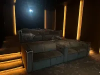 A dark home theater with rows of grey velvet sofas, ambient floor-level lighting, and a projector screen in the back.