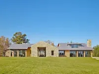 A modern, single-story stone house with a metal roof set against a clear blue sky on a grassy hill.
