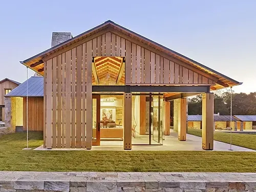 A modern home with vertical wood siding, a large glass facade, and a metal roof at dusk.