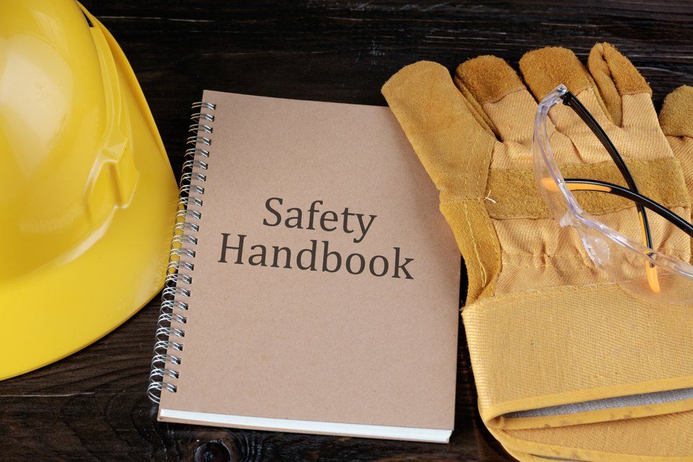 A Safety Handbook is Sitting on a Wooden Table Next to a Hard Hat and Gloves — Signtek Gladstone in Gladstone Central, QLD