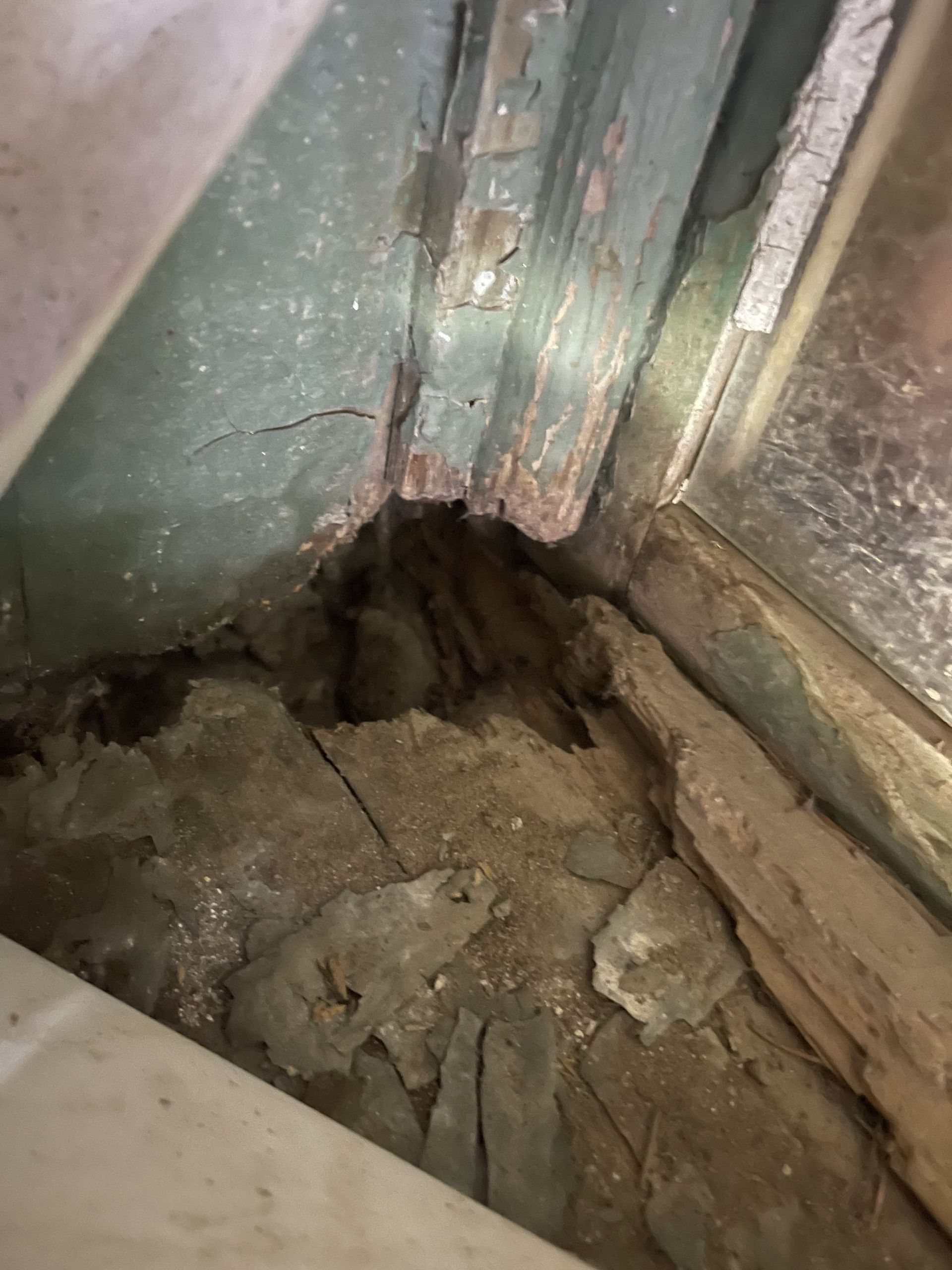 A hole in the floor of a building next to a window.