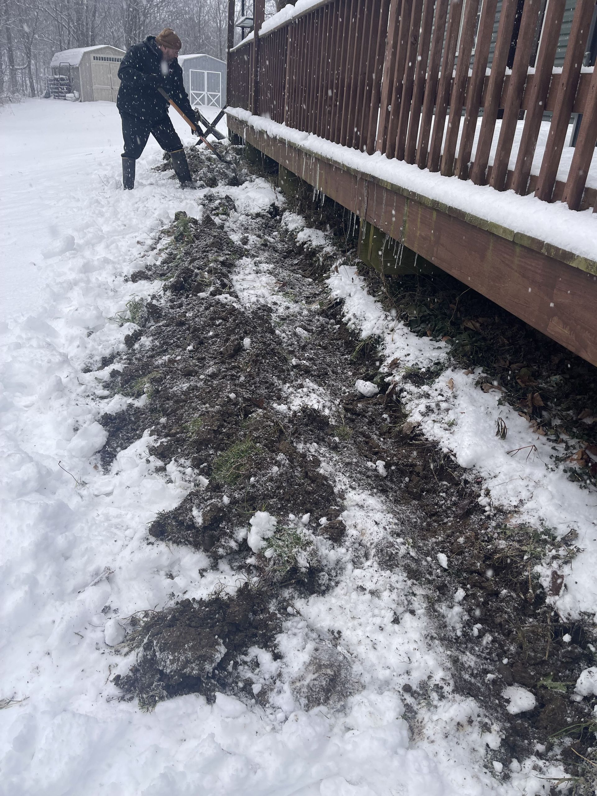 A man is shoveling snow next to a deck.