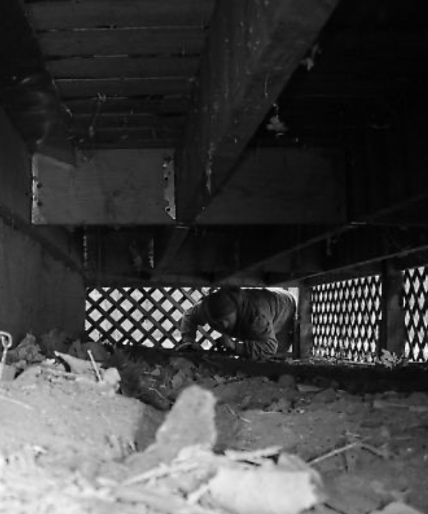 A black and white photo of a man crawling under a bridge.