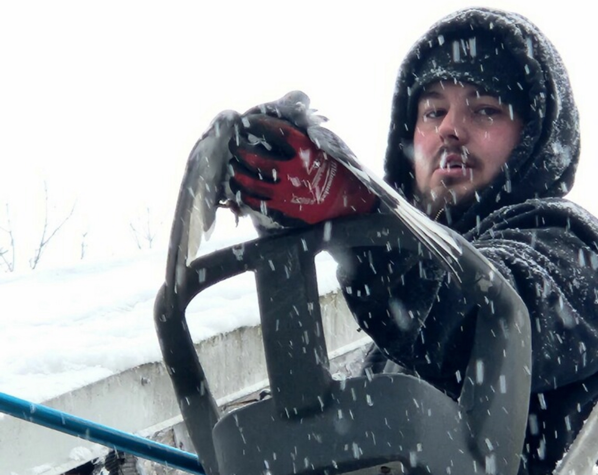 A man is driving a boat in the snow and holding a fish in his hand.