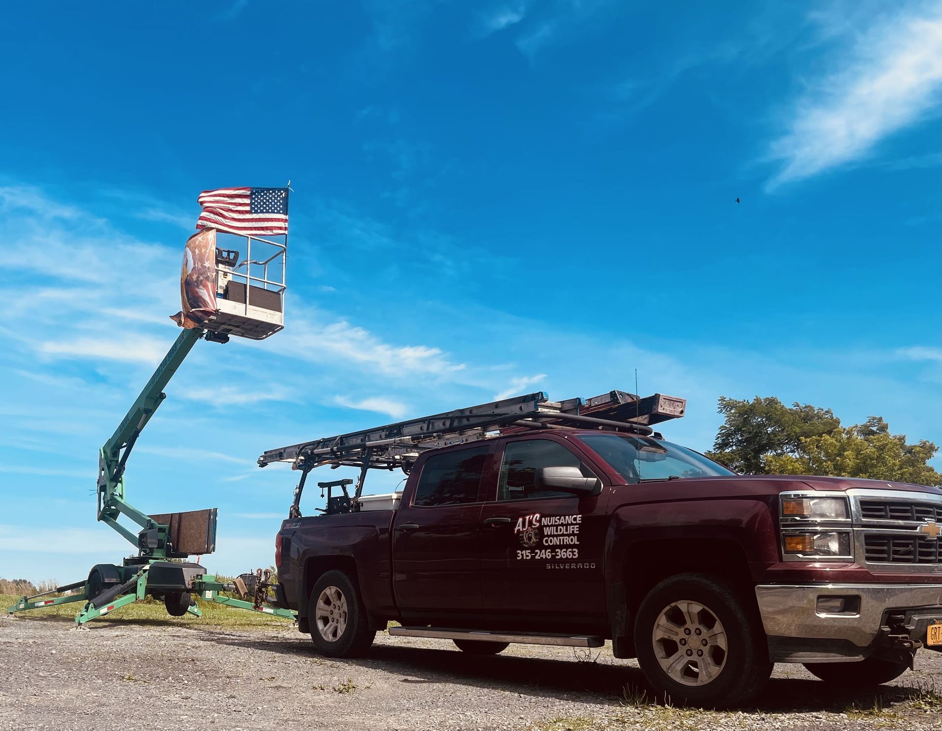 A truck with a ladder on the back is parked next to a crane with an american flag on it.