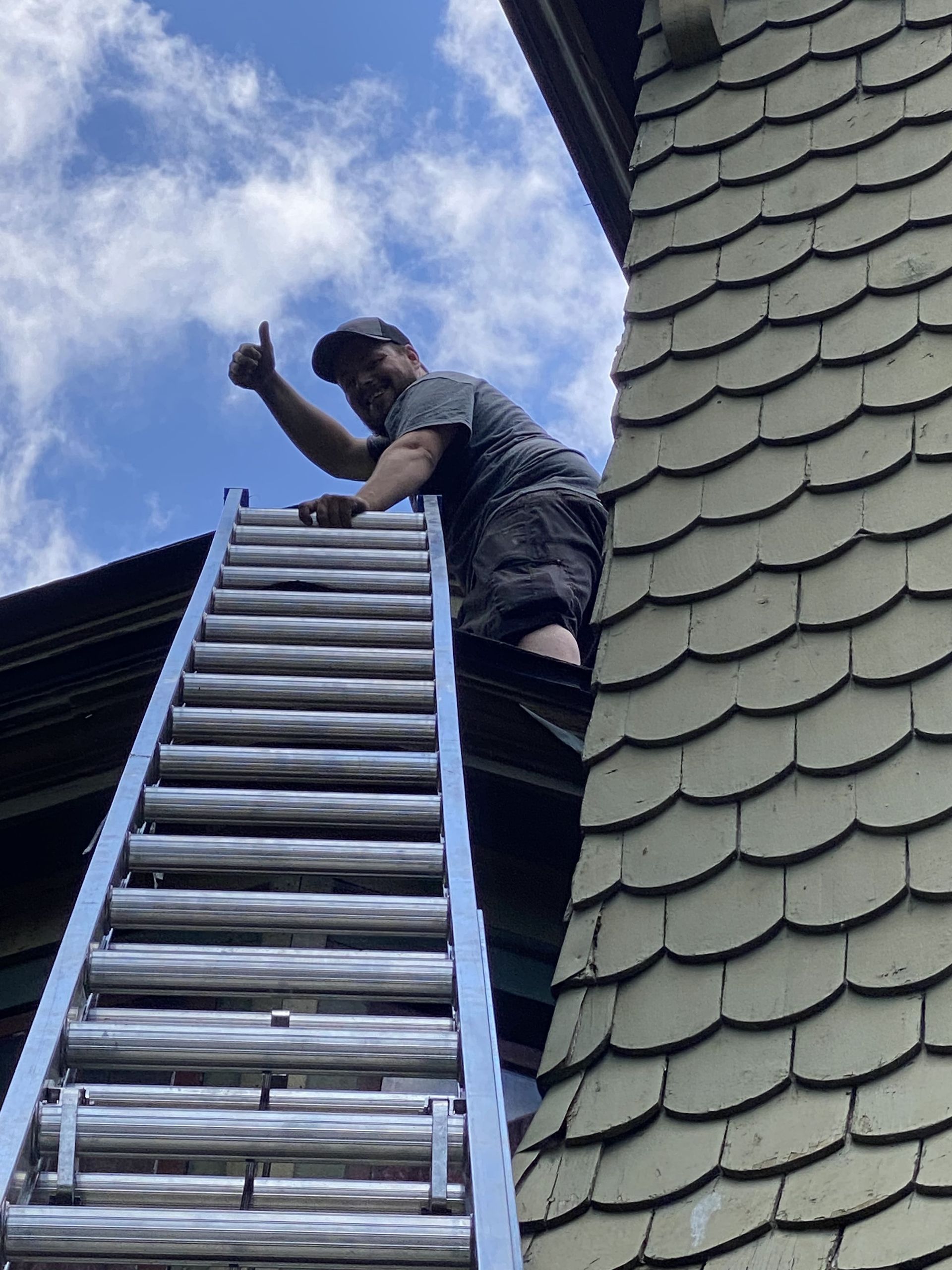 A man is climbing up a ladder on the side of a building.