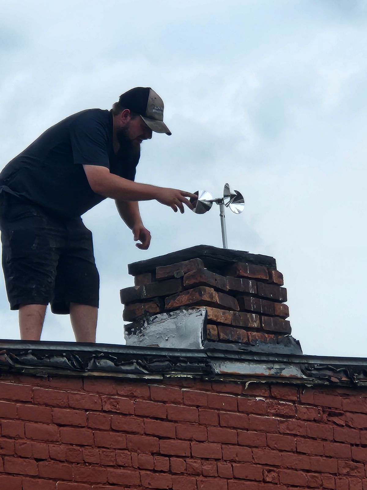 A man is working on a chimney on top of a brick building.