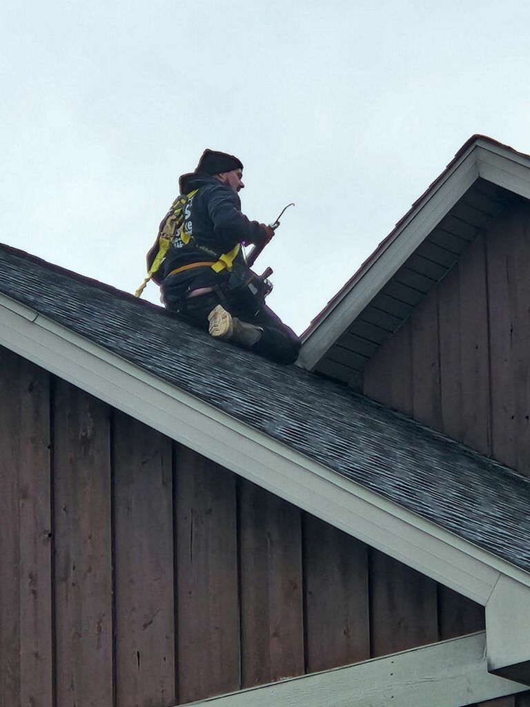 A man is sitting on the roof of a building holding a tool.