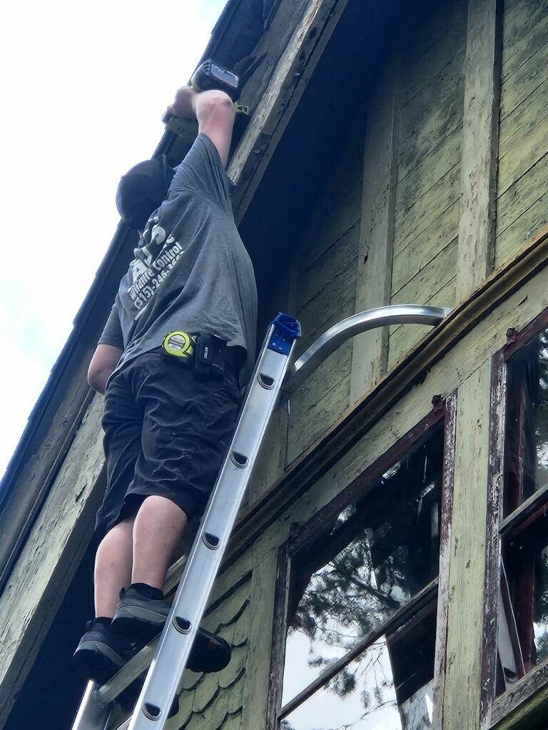 A man is standing on a ladder on the side of a building.