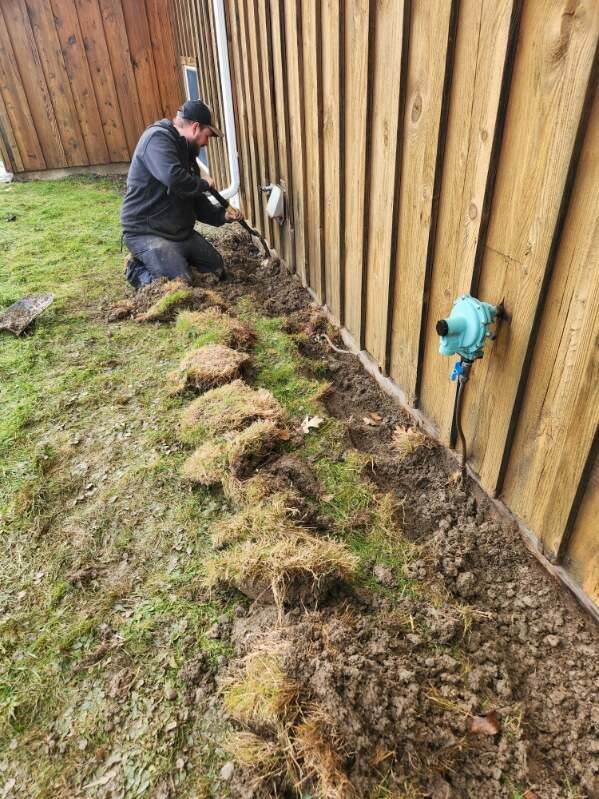 A man is digging a hole in the ground next to a wooden fence.