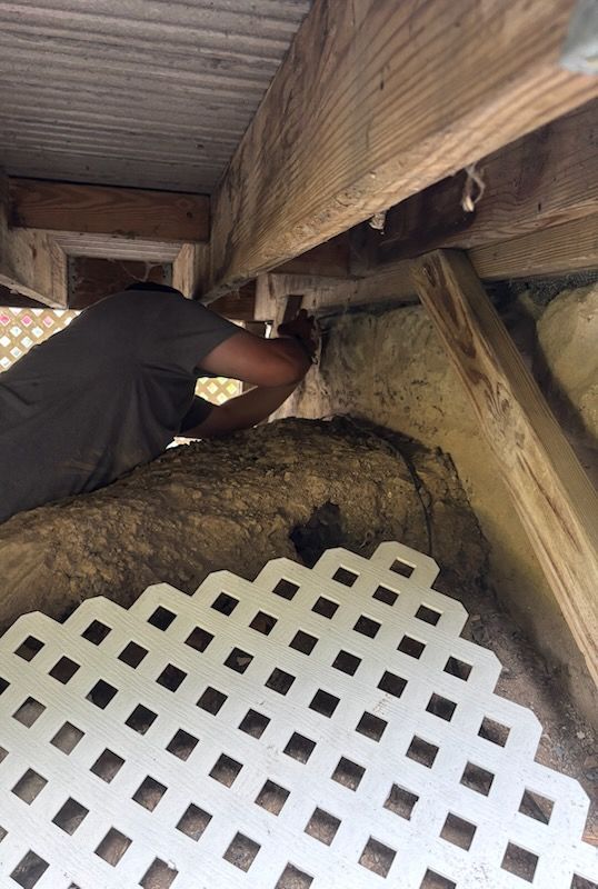Person working under a wooden structure, possibly repairing, with white lattice nearby.