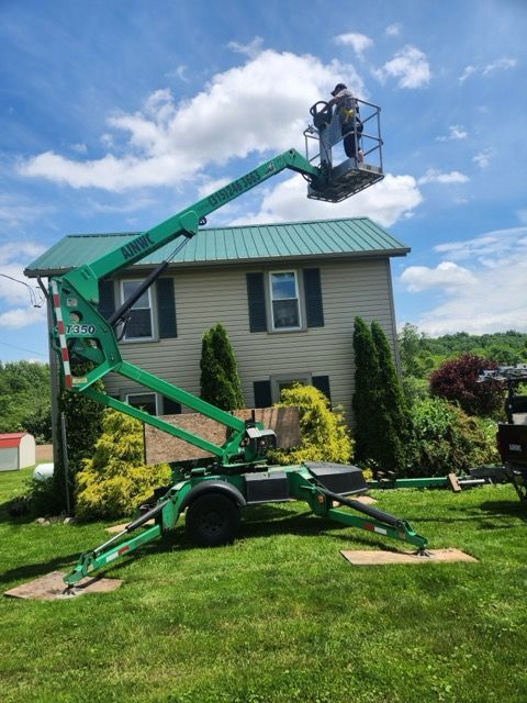 A man in a lift basket near a house; green lift, blue sky.