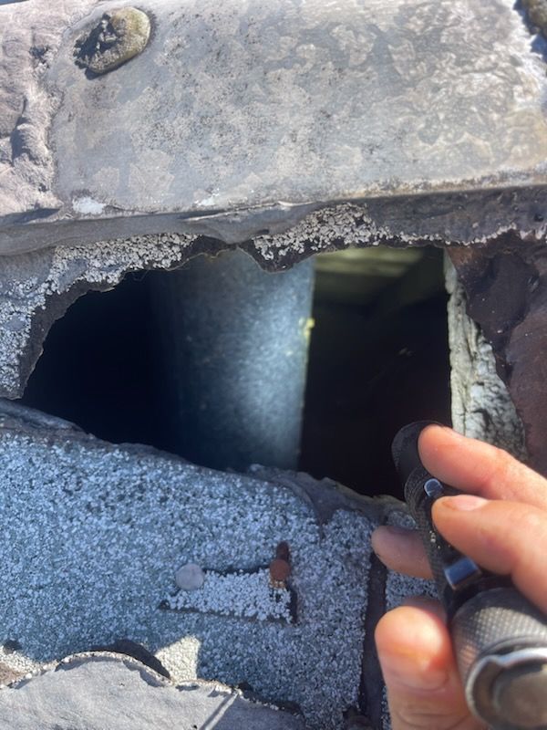 A person shines a flashlight into a dark chimney opening on a roof.