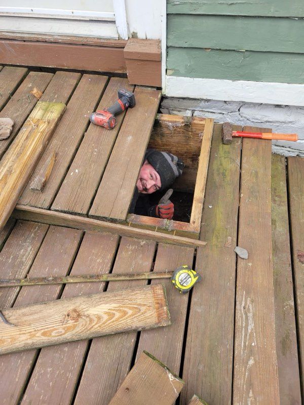 Man inside deck's access panel, tools scattered. Deck boards are broken.