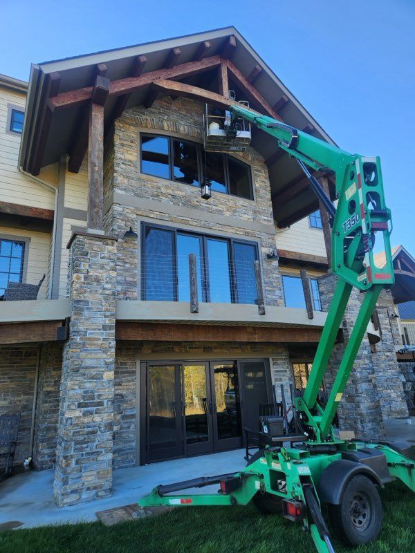 Green lift reaching towards a two-story house with stone and tan siding.