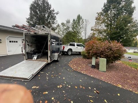 White truck pulling a trailer with the ramp down in a driveway. Overcast sky.