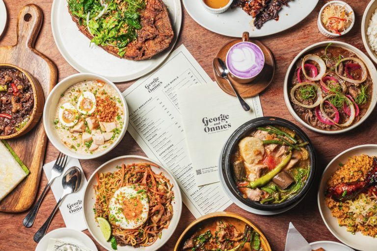 Overhead shot of a table laden with Filipino dishes: adobo, pansit, soup, fried chicken, and more.