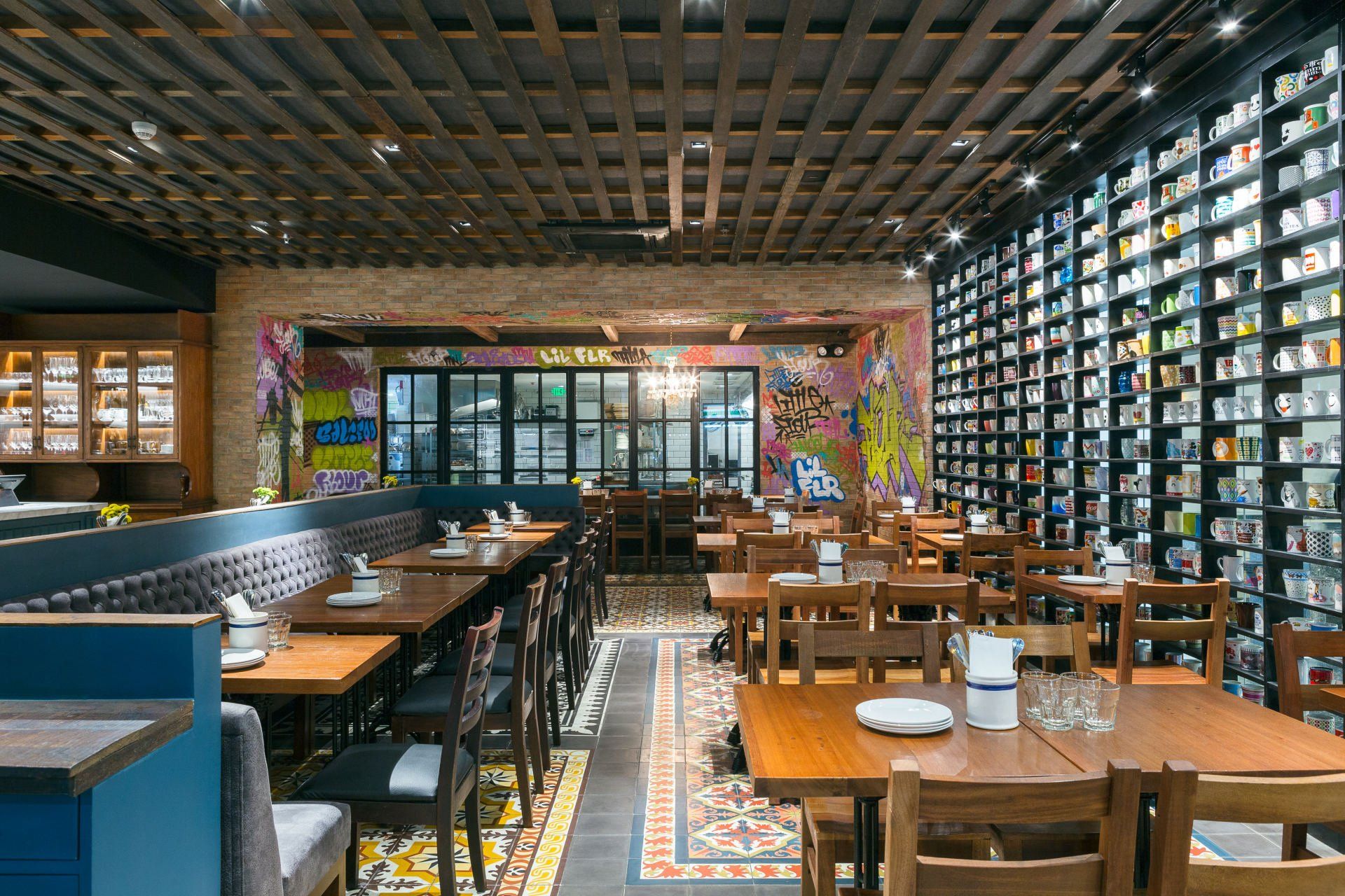 Restaurant interior with wooden tables, brick walls, and a wall of shelves; colorful graffiti art.