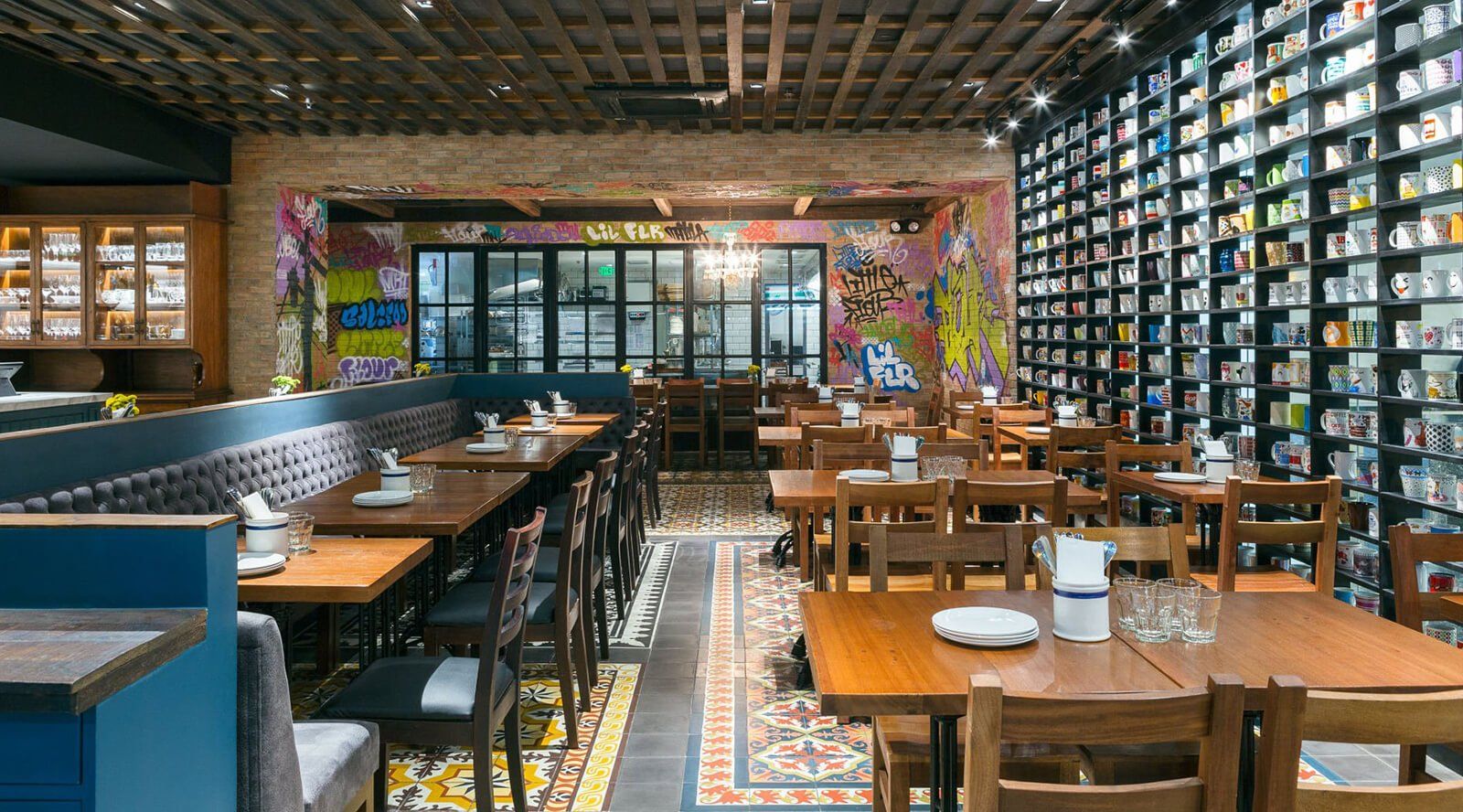 Restaurant interior: wooden tables, chairs, colorful wall art, and a wall of framed objects.