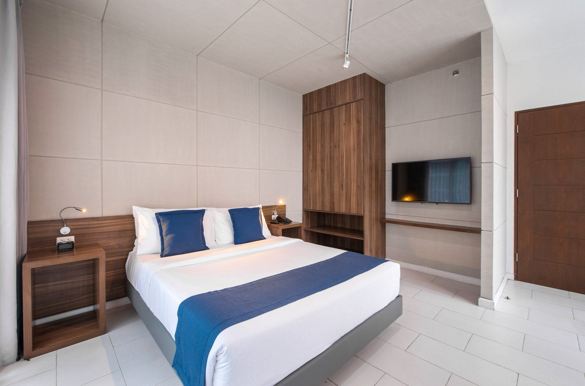 Modern hotel bedroom with a bed, wooden closet, and TV.