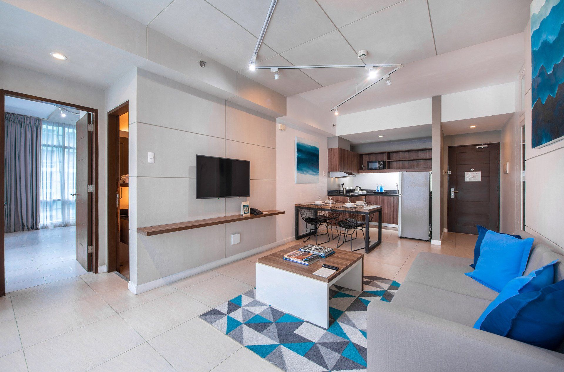 Modern apartment living room with TV, kitchen, and blue accents.