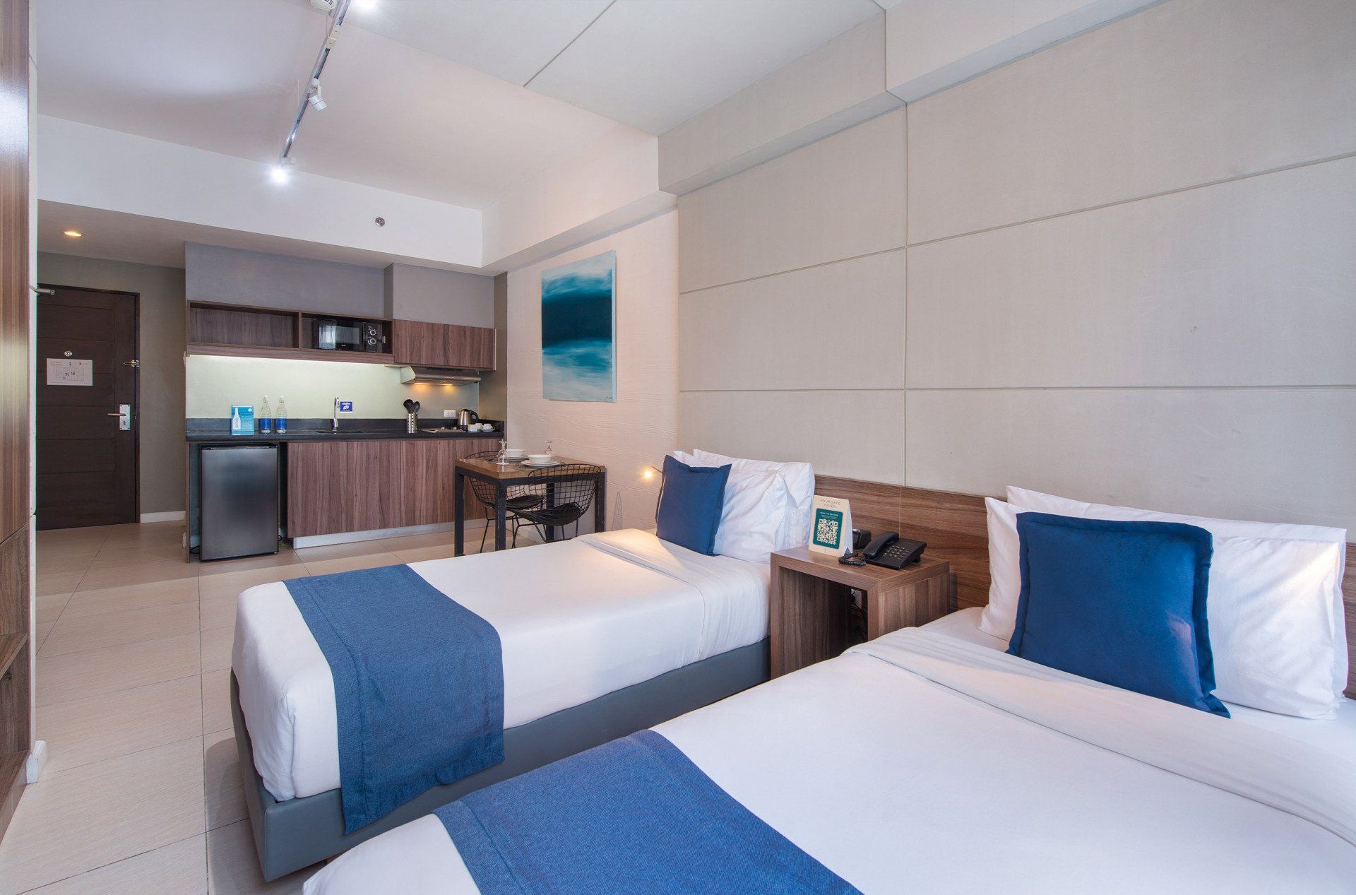 Two twin beds in a modern hotel room with a small kitchenette.
