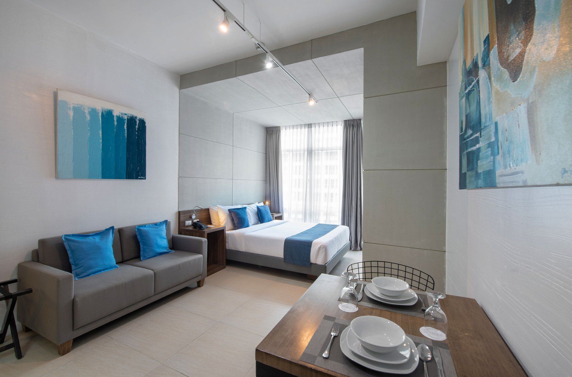 Modern studio apartment with living, sleeping, and dining areas. Gray sofa with blue pillows, a bed, and a dining table.