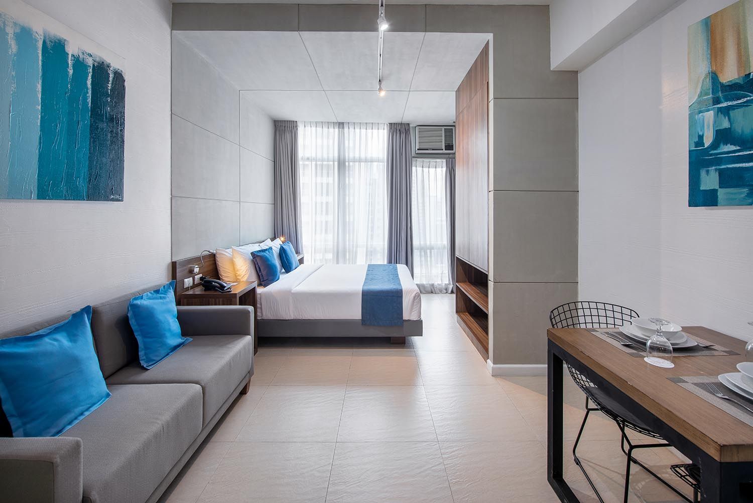 Modern studio apartment with a bed, sofa, and dining table. Blue and gray color scheme.