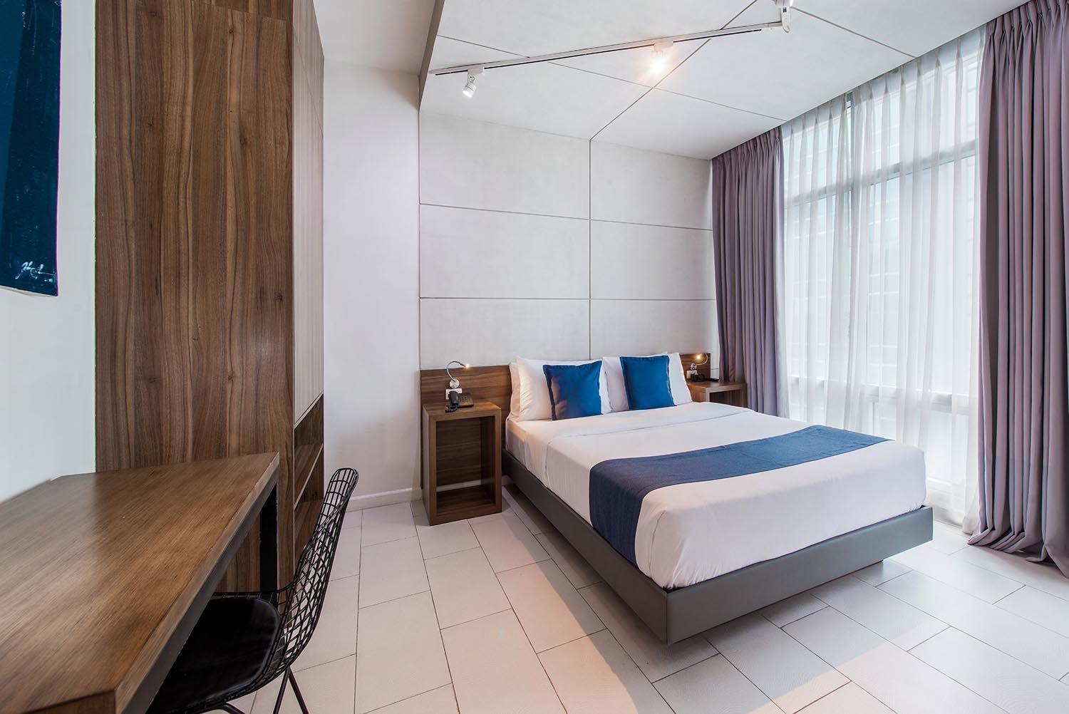 Modern hotel bedroom with bed, desk, and large window with purple curtains.