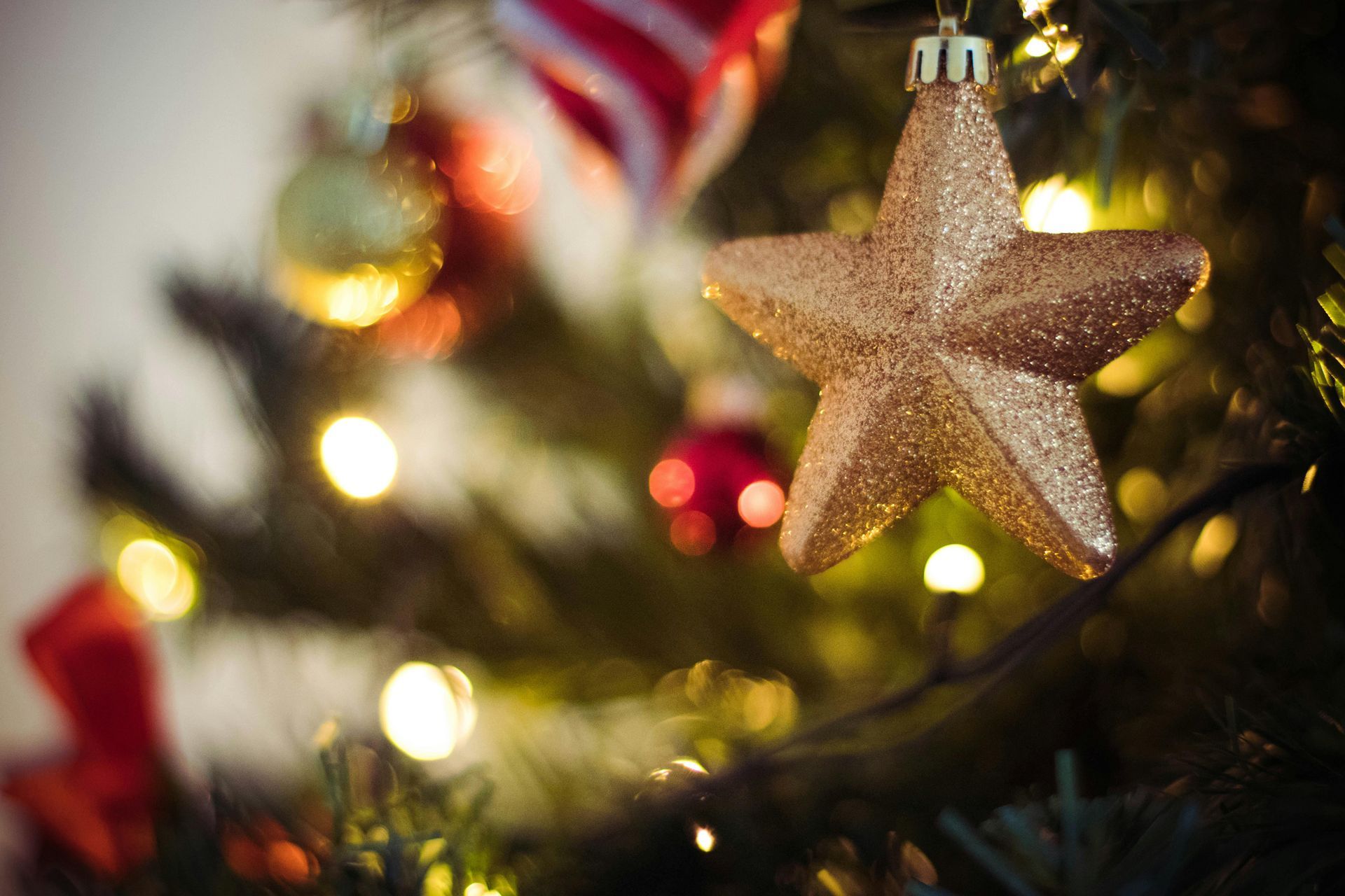 Golden star ornament on a decorated Christmas tree, with blurred lights and other ornaments.