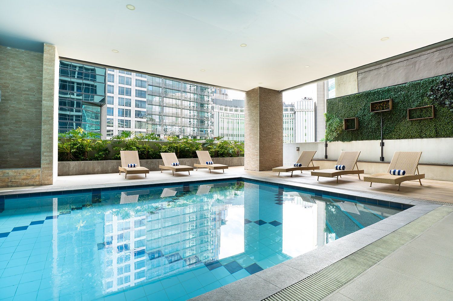 Indoor pool with lounge chairs, cityscape view, and a wall of greenery.