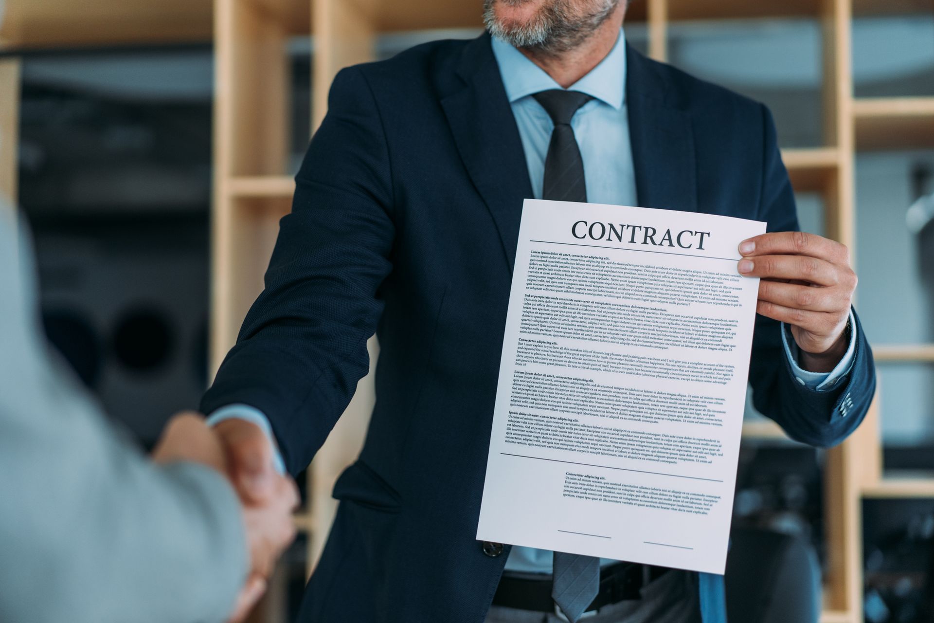 Man in suit holding a contract, shaking hands with another person.