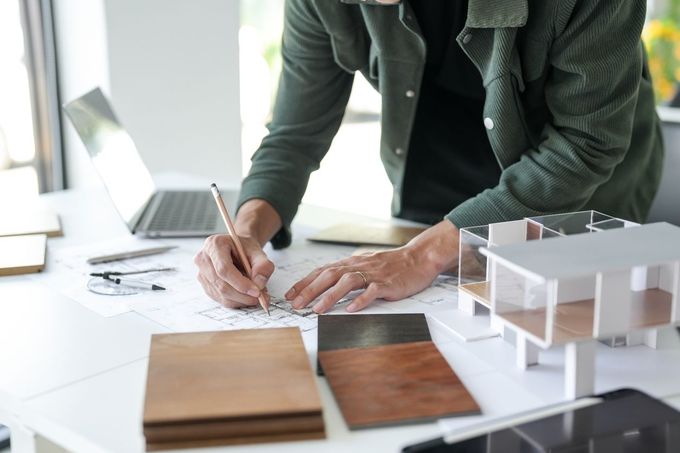A man is sitting at a table drawing a model of a house.