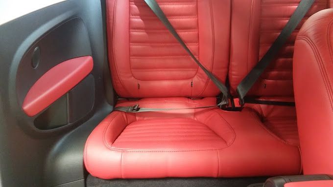 The back seat of a car with red seats and black seat belts.