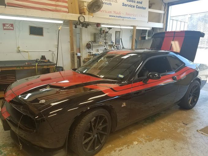 A black and red dodge challenger is parked in a garage with the hood up.