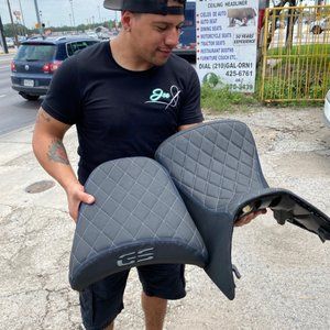 A man is holding two motorcycle seats in his hands.