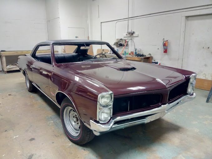 A burgundy muscle car is parked in a garage