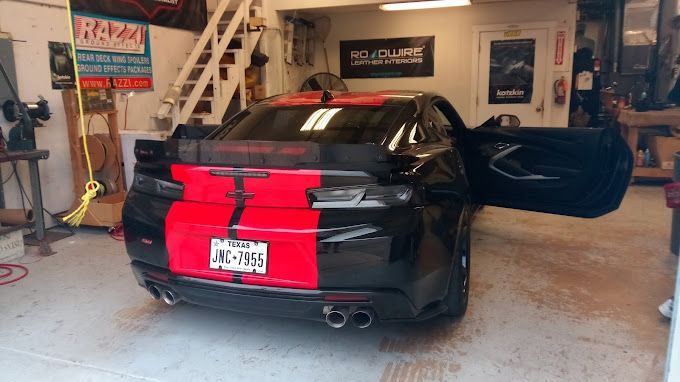 A black and red car is parked in a garage with its doors open.