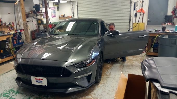 A man is standing next to a gray mustang in a garage.